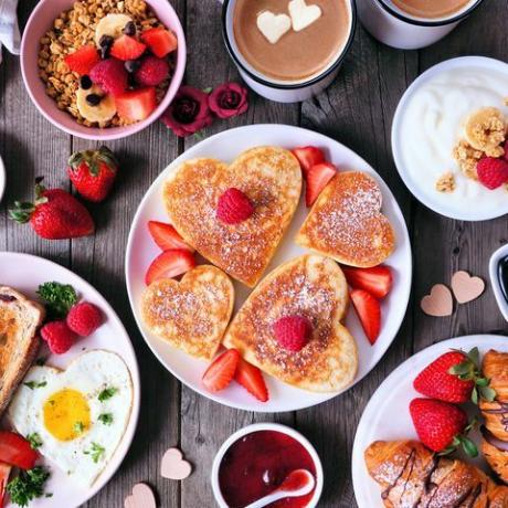 Сцена на маса за закуска за Свети Валентин или Деня на майките на фон от тъмно дърво с палачинки във формата на сърце, яйца и любовна тематична храна