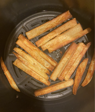 снимка отгоре на кошницата за готвене на ninja air max xl air fryer, която съдържа предимно златистокафяви ръчно нарязани пържени картофи